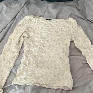 Beige långärmad topp från Gina Tricot - Säljer en beige långärmad topp från Gina Tricot i storlek XS. Toppen har ett unikt strukturerat mönster med 3D-effekt och är tillverkad i ett lätt, transparent material. Den har en rund halsringning, perfekt för dig som gillar trendiga och annorlunda plagg!