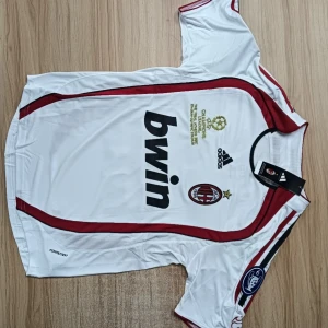 AC Milan Kaka' 22 vit Adidas tröja S - AC Milan fotbollströja med Kaka' 22 på ryggen, officiell Adidas med Champions League-märke och Bwin sponsor. Vit med röda detaljer och svarta inslag, kortärmad och tillverkad i lätt, ventilerande polyester. Snygga ränder längs axlarna och klubbmärke på bröstet.