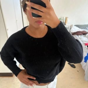 Svart stickad tröja med rund hals - En svart stickad tröja med rund halsringning och långa ärmar. Tröjan har en klassisk, enkel design och är lite loose i passformen. Perfekt att slänga på sig när det är kyligt ute. Passar till allt och är superenkel att styla.