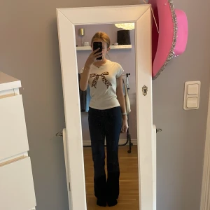 Vit t-shirt med leopardrosett Stradivarius - Vit t-shirt från Stradivarius i bomull med korta ärmar och en stor rosett framtill i leopardmönster. Klassisk rund halsringning och figurnära passform. Perfekt för dig som vill ha en söt men edgy vibe.