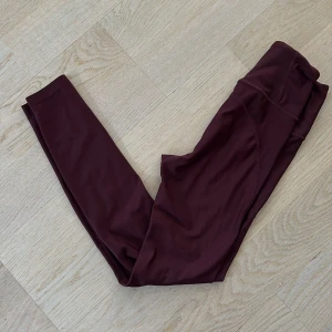 Vinröda tights från Energetics XS - Supersnygga vinröda tights från Energetics i storlek XS. De är högmidjade och gjorda i ett stretchigt syntetmaterial med DryPlus-teknologi som andas. Perfekta för träning eller chill, med en tight passform och mjuk känsla.