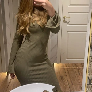 Ribbad långärmad klänning H&M XS - Snygg ribbad långklänning från H&M i en beige/grön ton. Klänningen har lång ärm, hög hals och figurnära passform som framhäver siluetten. Perfekt för dig som gillar stilrena och enkla plagg med lite edge. Materialet är mjukt och stretchigt, troligen bomull med inslag av syntet.