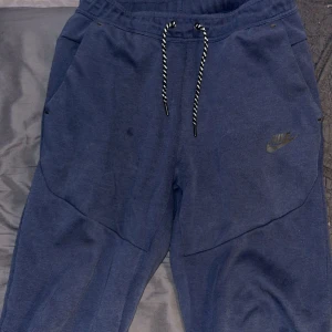 Blå mjukisbyxor från Nike, stl S - Mörkblå mjukisbyxor från Nike med dragsko i midjan och diskret Nike-logga på benet. Byxorna har muddar vid bensluten och är tillverkade i mjukt bomullsmaterial. Perfekta för chill eller träning.