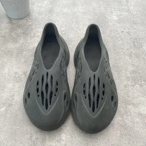 Adidas Yeezy Foam Runner svart - Säljer ett par Adidas Yeezy Foam Runner i svart. Skorna har en futuristisk design med massor av hål för ventilation och är gjorda i ett lätt syntetmaterial. Perfekta för dig som vill ha något unikt och bekvämt på fötterna.