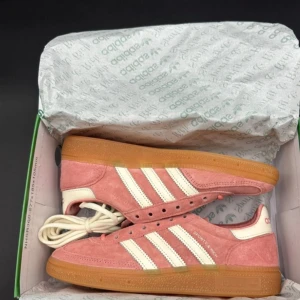 Adidas Samba Sporty & Rich rosa mocka - Adidas Samba Sporty & Rich i rosa mocka med klassiska vita ränder och gummisula. Skorna har snörning och detaljer i krämvitt, samt branding på plösen och hälen. Perfekta för dig som vill sticka ut med en retrovibe och snygg färgkombo.