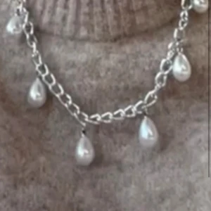 Silverhalsband med droppformade pärlor - Stilrent halsband i silverfärgad kedja med hängande droppformade pärlor. Kedjan har grova länkar som ger ett coolt uttryck och pärlorna ger en elegant touch. Perfekt för att lyfta din outfit med lite extra bling.