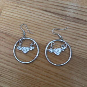Silvriga örhängen med hjärta och vingar - Coola silvriga örhängen i form av stora ringar med ett detaljerat hjärta med vingar hängande i mitten. Perfekta för dig som vill sticka ut och addera lite edge till din stil.