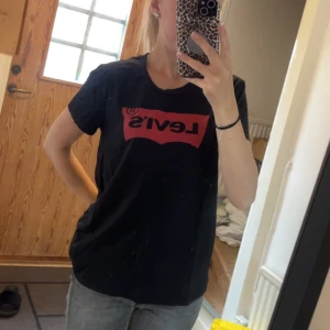 Svart Levi's t-shirt med röd logga - Svart t-shirt från Levi's med klassisk röd logga framtill. Modellen är normal passform med rund hals och korta ärmar. Materialet är mjuk bomull som känns skön mot huden. Perfekt till jeans eller shorts för en chill look.