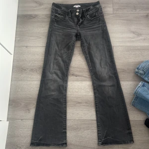 Svarta bootcut jeans från Gina Tricot - Snygga svarta bootcut jeans från Gina Tricot i storlek 158. Jeansen har en cool tvättad look, vita kontrastsömmar och dubbla knappar framtill. Klassisk femficksmodell med extra ficklock och silverfärgade detaljer. Perfekta för en trendig vardagsstil.