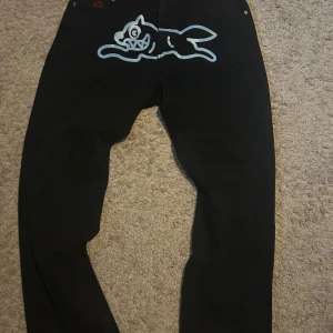  Icecream svarta jeans med print - Säljer ett par svarta jeans från  Icecream med ett stort, vitt grafiskt print av en tecknad hund på baksidan. Jeansen har klassisk femficksdesign och är gjorda i slitstarkt bomullsmaterial. Perfekt för dig som gillar streetwear och unika detaljer.