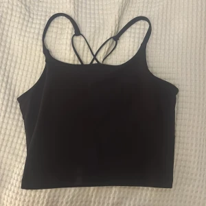 Mörk lila croppad träningstopp - En svart croppad linnetopp med smala axelband som korsas i ryggen. Perfekt till träning eller vardag.(ser svart ut på bilden men den är mörkröd/lila)