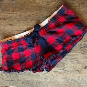 Röd- och marinblå rutiga shorts Hollister - Supermysiga rutiga shorts från Hollister i rött och marinblått. De har en bred resår i midjan med en stor marinblå rosett framtill och volangkant nertill. Perfekta för chill dagar eller som pyjamasshorts. Passar perfekt både till hösten men också vintern 