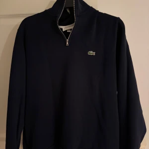 Marinblå half zip tröja från Lacoste - Snygg marinblå långärmad tröja från Lacoste med half zip. Perfekt för dig som gillar stilrena och sportiga plagg. Skön passform och enkel att matcha med det mesta. Pris kan diskuteras