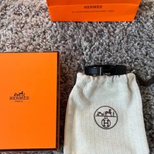 Svart H-berlock armband från Hermès - Stilrent svart armband från Hermès med den ikoniska H-berlocken i metall. Kommer med original ask och dustbag i klassisk orange Hermès-färg. Så allt og följer med! Digitalt kvitto finns även! Skicka bud