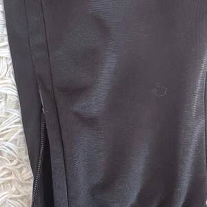 Svarta träningsbyxor från Puma - Svarta träningsbyxor från Puma med klassisk logga på benet. Byxorna har dragkedja vid benslut och är gjorda i ett stretchigt syntetmaterial som passar perfekt för sport och aktivitet. Snygg och sportig look med smal passform.