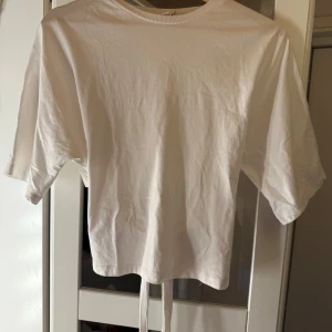 Vit Nelly t-shirt  - Säljer trendiga T-shirten från Nelly med knyte i ryggen i strl M, passar S och eventuellt L också!🤍 supersnygg och inga defekter, skriv för fler bilder eller vid frågor!😊