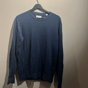 Mörkblå stickad  tröja från Jack & Jones storlek S - En stilren mörkblå långärmad tröja från Jack & Jones i storlek S. Tröjan har rund halsringning och är tillverkad i ett mjukt material som passar perfekt till lager-på-lager. Enkel och clean design utan mönster eller detaljer.