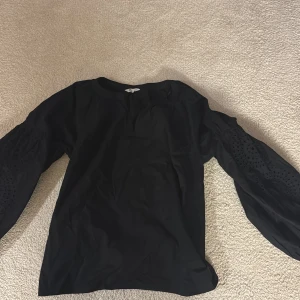 Svart blus med broderade ärmar - Svart blus från Cubus i storlek S med unika broderade detaljer på de långa ärmarna. Ärmarna har knäppning vid mudden och ett snyggt cirkelmönster som ger en cool vibe. Blusen är gjord i mjuk bomull och har en relaxed passform pris kan diskuteras!🩷.