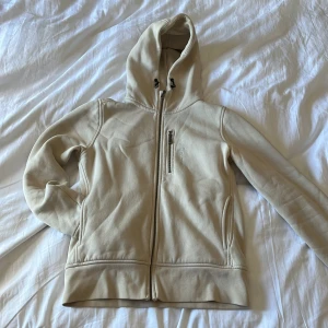 Beige hoodie från Sail Racing, S - Snygg beige hoodie från Sail Racing med dragkedja framtill och bröstficka med zip. Mjuk insida och huva med snörning. Perfekt för kyliga dagar och enkel att matcha med jeans eller joggers.(behövs strykas)