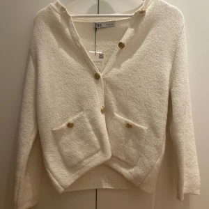 Vit kofta från Zara - Superfin vit kofta från Zara med snygga guldknappar och två fickor framtill. Koftan har en mjuk, stickad känsla och långärmad passform. Helt oanvänd med prislappen kvar! Perfekt för lager-på-lager och ger en clean look till din outfit!💕