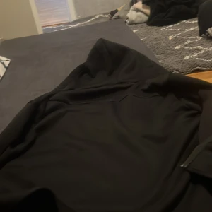 Svart vindjacka med huva - Svart vindjacka med huva, perfekt för blåsiga dagar. Jackan har en enkel och stilren design utan synliga mönster eller detaljer. Passar dig som gillar en clean look och vill ha något lätt att slänga på sig.