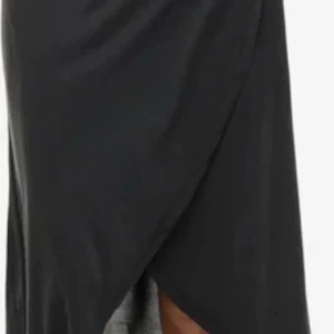 Svart omlottkjol från Vila - Svart långkjol från Vila i omlottmodell med snygg drapering framtill. Kjolen är tillverkad i ett mjukt och följsamt material som ger en clean och stilren look. Perfekt för dig som gillar minimalistisk stil och vill ha något enkelt men ändå trendigt.