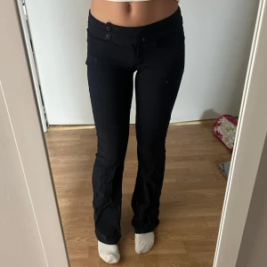 Mörkblå bootcut byxor - Mörka bootcut byxor med två snygga knappar i midjan. Byxorna har låg midja och är tillverkade i ett stretchigt material av viskos, nylon och spandex. De är i storlek small och är bootcut 💙