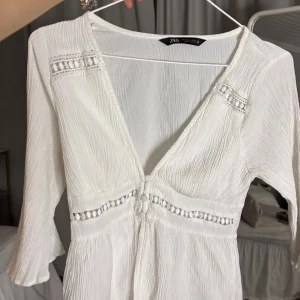 Vit blus från Zara - Superfin vit blus från Zara med v-ringning, knappar framtill och spetsdetaljer vid byst och midja. Blusen har trekvartsärm och är gjord i ett lätt, krinklat material som känns luftigt och bekvämt. 