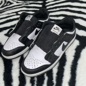Nike SB Dunk Low Pro svart/vit - Nike SB Dunk Low Pro sneakers i svart och vitt med klassisk låg siluett. Skorna har perforerad tå, platt sula och ikonisk Swoosh på sidan. Ovandelen är i skinn och textil, med snörning och vadderad plös för extra komfort. Perfekt för dig som gillar streetstyle och skate.