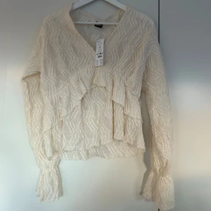 Vit blus med volangdetaljer - Säljer en superfin vit blus från Ginatricot i storlek M. Säljer den eftersom jag beställde den i fel storlek och den togs bort från sortimentet. Den har ett snyggt volangmönster och långa ärmar med volangdetaljer vid ärmsluten. Perfekt för både vardag och fest! ✨