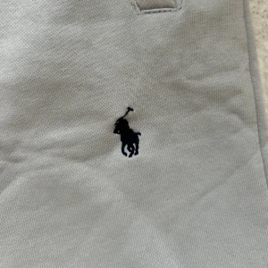 Grå mjukisbyxor Polo Ralph Lauren - Snygga grå mjukisbyxor från Polo Ralph Lauren i storlek M. Byxorna har ribbad midja med snörning, två sidofickor och den klassiska broderade Polo-loggan på benet. Tillverkade i mjukt bomullsmaterial som är skönt mot huden.
