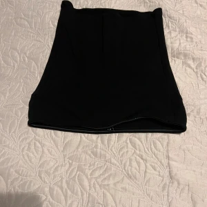 Svart tube top - Snygg svart tube top med tight passform. Kjolen är enkel och stilren utan synliga detaljer eller mönster, perfekt för dig som gillar minimalistisk stil. Materialet känns mjukt och stretchigt, vilket gör den bekväm att bära hela dagen.