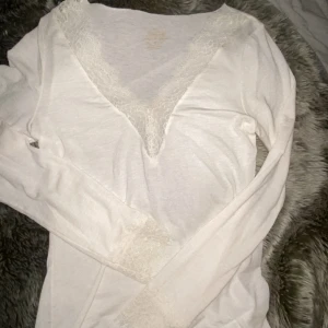 helt ny vit intimissmi tröja  - Säljer en vit långärmad topp med snygg v-ringning och spetsdetaljer vid halsen och ärmsluten. Modellen är figurnära och har en mjuk, stretchig känsla som sitter skönt mot kroppen. 