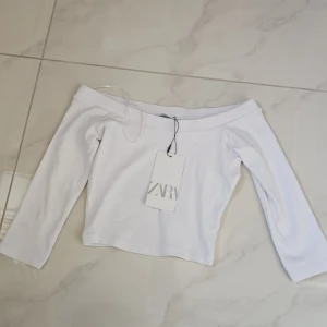 Vit offshoulder topp från Zara - Supersnygg vit offshoulder topp från Zara i ribbad bomull. Croppad modell med långa ärmar som ger en clean och fräsch vibe. Perfekt för dig som gillar minimalistisk stil och vill ha något som sticker ut med sin axelbara design.