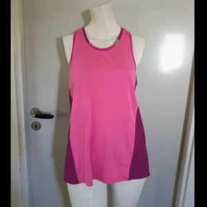 Rosa och lila träningstopp - Sportig linnetopp i två nyanser av rosa och lila, perfekt för gymmet eller löprundan. Modellen är ärmlös med brottarrygg och har en loose passform som ger skön rörelsefrihet. Materialet är lätt och andas, vilket gör den grym för svettiga pass.