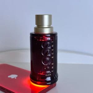 Boss The Scent Elixir 50ml parfym - Öppen för trade. Boss The Scent Elixir är en elegant herrparfym i en mörkröd glasflaska med guldigt sprayhuvud och lock. Flaskan rymmer 50 ml och har en stilren, cylindrisk form med tydlig Boss-logga i relief. Perfekt för dig som gillar exklusiva dofter och snygg design. Runt 48ml kvarstår.