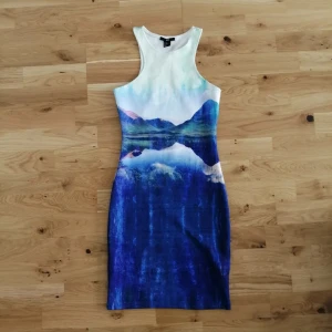 Blå kortklänning med landskapsmotiv - Tight kortklänning från H&M med coolt landskapsmotiv i blå och vita toner. Klänningen är ärmlös med rund hals och har en snygg öppen rygg. Materialet är stretchigt och följer kroppen perfekt. 