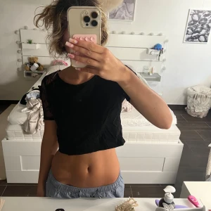 Svart croppad spets-topp - Säljer en svart croppad blus med korta ärmar i genomskinlig spets. Toppen har rund halsringning och coola spetsdetaljer både fram och på ärmarna. Den är från hm och är i st 38.