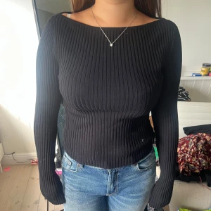 Svart ribbad långärmad tröja - Säljer en svart, ribbad långärmad tröja med tight passform och bred halsringning. Tröjan är stretchig och sitter snyggt mot kroppen, perfekt till jeans eller kjol. Materialet känns mjukt och följsamt, och den har en stilren look som funkar till många olika outfits.