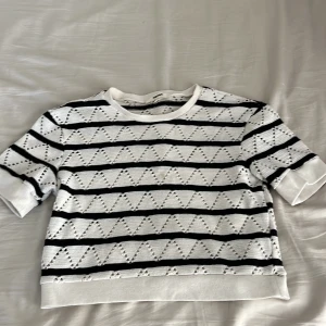 Vit och svart stickad tröja Koton - Säljer en vit och svart stickad tröja från Koton i storlek L. Tröjan har korta ärmar och ett snyggt hålmönster med svarta ränder och zigzag-detaljer. Ribbad kant vid ärmslut och nederkant. Perfekt för dig som gillar grafiska mönster och chill stil.