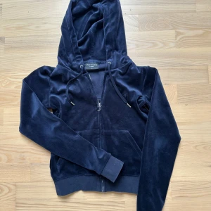 Mörkblå velour hoodie Juicy Couture - Säljer en mörkblå hoodie från Juicy Couture i mjuk velour med dragkedja och snörning vid huvan. Tröjan har långa ärmar och en klassisk känguruficka framtill. Perfekt för dig som gillar comfy och trendigt.
