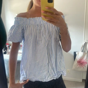 Blåvit offshoulder randig topp - Säljer en söt offshoulder topp med blå och vita ränder. Toppen har korta puffärmar och en smockad kant upptill som ger en chill och somrig vibe. Perfekt för dig som gillar en luftig och avslappnad stil. Materialet känns lätt och bekvämt mot huden. Storlek S/m men sitter bra på mig med xs/s också