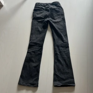 Bootcut jeans från Gina Tricot - Snygga svarta bootcut jeans från Gina Tricot med klassisk femficksdesign och knappstängning. Jeansen har en mörk tvätt och är tillverkade i ett mjukt bomullsmaterial med lite stretch för extra komfort. Perfekt för dig som gillar en retro vibe och vill ha ett par jeans med lite utsvängda ben.