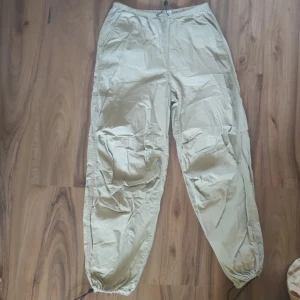 Beige cargopants från H&M Divided XXS - Snygga beige cargopants från H&M Divided i storlek XS. Byxorna har elastisk midja och snörning vid bensluten för en cool look. Tillverkade i lätt polyester, med fickor både fram och bak. Perfekta för en avslappnad streetstyle.