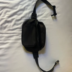 Svart axelväska med dragkedja  - Svart axelväska från Geox i syntetmaterial med justerbart band och smidig plastspänne. Väskan har ett stort huvudfack med dragkedja och en mindre ficka framtill, perfekt för mobilen och småprylar. Enkel och clean design som funkar till alla outfits. Använd 1/2 gånger!
