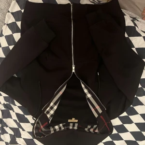 Svart Burberry bomberjacka XL, sitter som en L  - Svart bomberjacka från Burberry i storlek XL. Jackan har klassiskt rutigt foder, silverfärgad dragkedja och ribbade muddar, e. Snygg och tidlös design med långärmade ärmar och detaljer som sticker ut. Perfekt för dig som vill ha en ikonisk look. Pris kan diskuteras, 