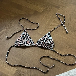Leopardmönstrad bikini med snörning - Snygg trekantsbikini med leopardmönster i svart, vit och rosa. Bikinin har tunna snören för knyt både i nacken och runt ryggen, vilket gör att du kan justera passformen enkelt. Perfekt för dig som vill sticka ut på stranden i sommar!