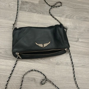 Svart axelväska från Zadig & Voltaire - Väskan är köpt för ca  3500 kr men säljer men säljer den för  1500 kr ❤️ Väskan har två dragkedjor och en mjuk, slouchy form som ger en avslappnad vibe. Perfekt för att bära dina essentials med stil. Älskar denna väskan men måste rensa mina saker💗 