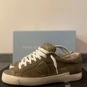 Olivgröna sneakers från Philippe Model - Säljer dessa fina olivgröna sneakers från Philippe Model med vit sula och vita snören. Skorna är i skinn och har en klassisk låg profil med rund tå och diskret logodetalj på sidan. Bra skick! Riktigt fina skor. Storlek 41. Allt org medföljer! Priset är diskuterbart. Nypris runt 3500 kr!