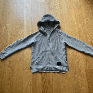 Grå ribbad hoodie från H&M - Säljer en grå ribbad hoodie från H&M i storlek 146/152. Tröjan har huva, half zip och en känguruficka framtill. Materialet är mjukt och stickat, perfekt för chill dagar. Långärmad och med snygga detaljer i ribbad struktur.